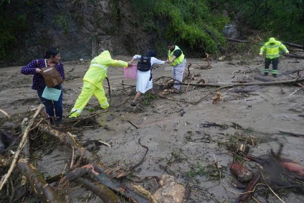 People get help crossing a highway blocked by a landslide triggered by Hurricane Otis near Acapulco, Mexico, on Oct. 25, 2023.